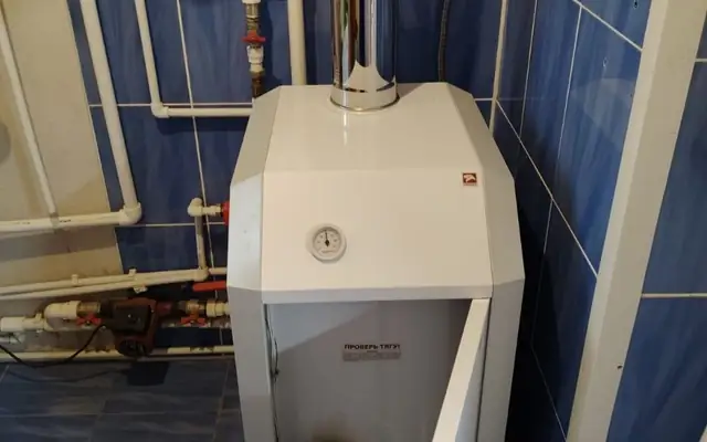 напольный газовый котёл с открытой фронтальной дверцей, видна верхняя панель с манометром, вертикальный дымоход и красный расширительный бак